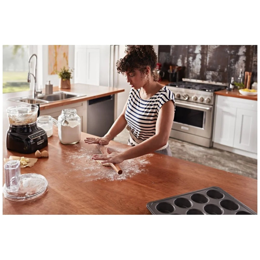 Lady baking in a kitchen with a freestanding gas range in the background. The range features a black porcelain-coated cooktop and stainless steel control knobs, with the oven in use to bake a delicious dish.