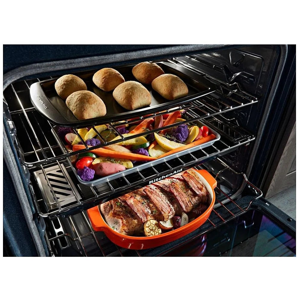 Close-up of food cooking on the KitchenAid KSGG700EBS gas slide-in range, showcasing burners in action with vibrant, sizzling ingredients.